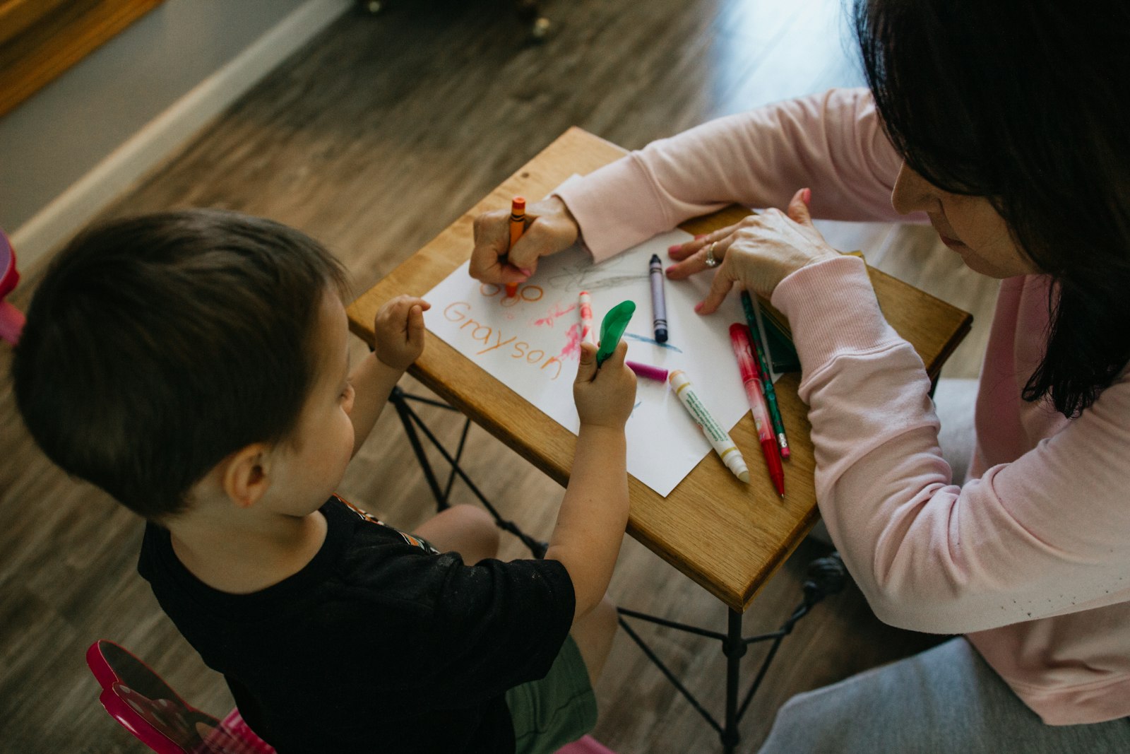 Teacher helping a child write their name with crayons